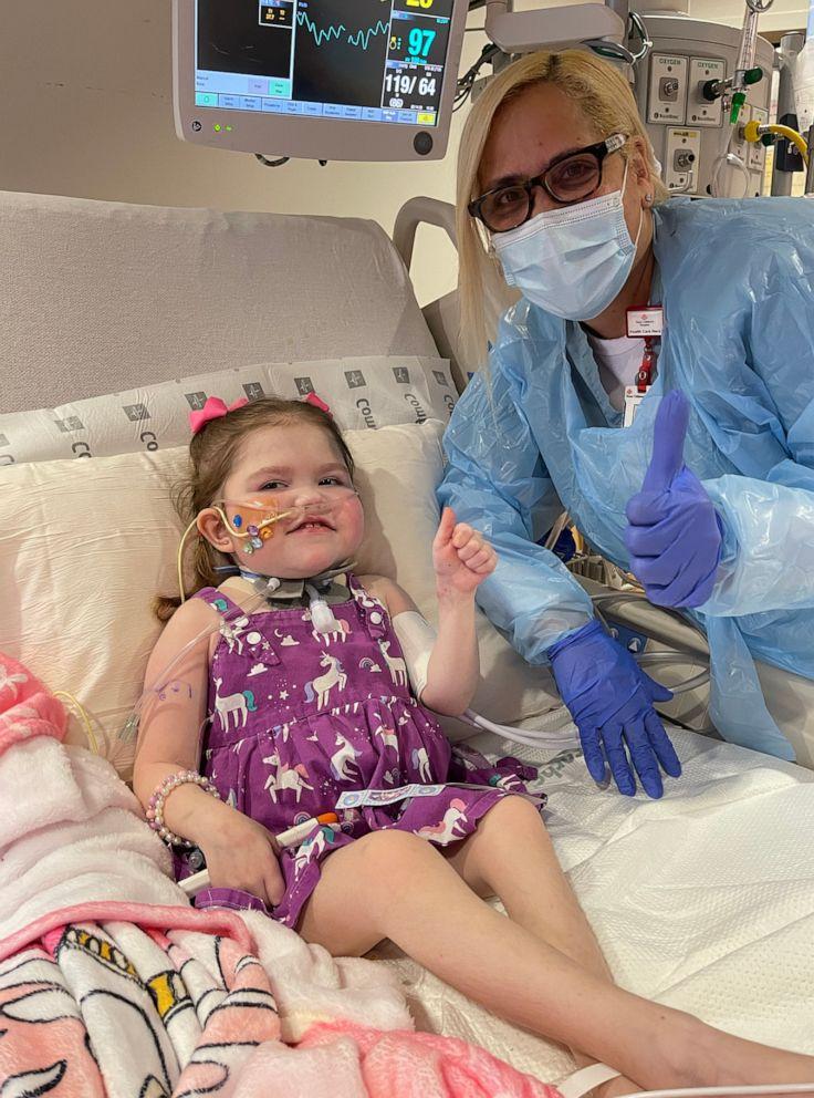 little girl in hospital bed and a doctor give thumbs up to camera