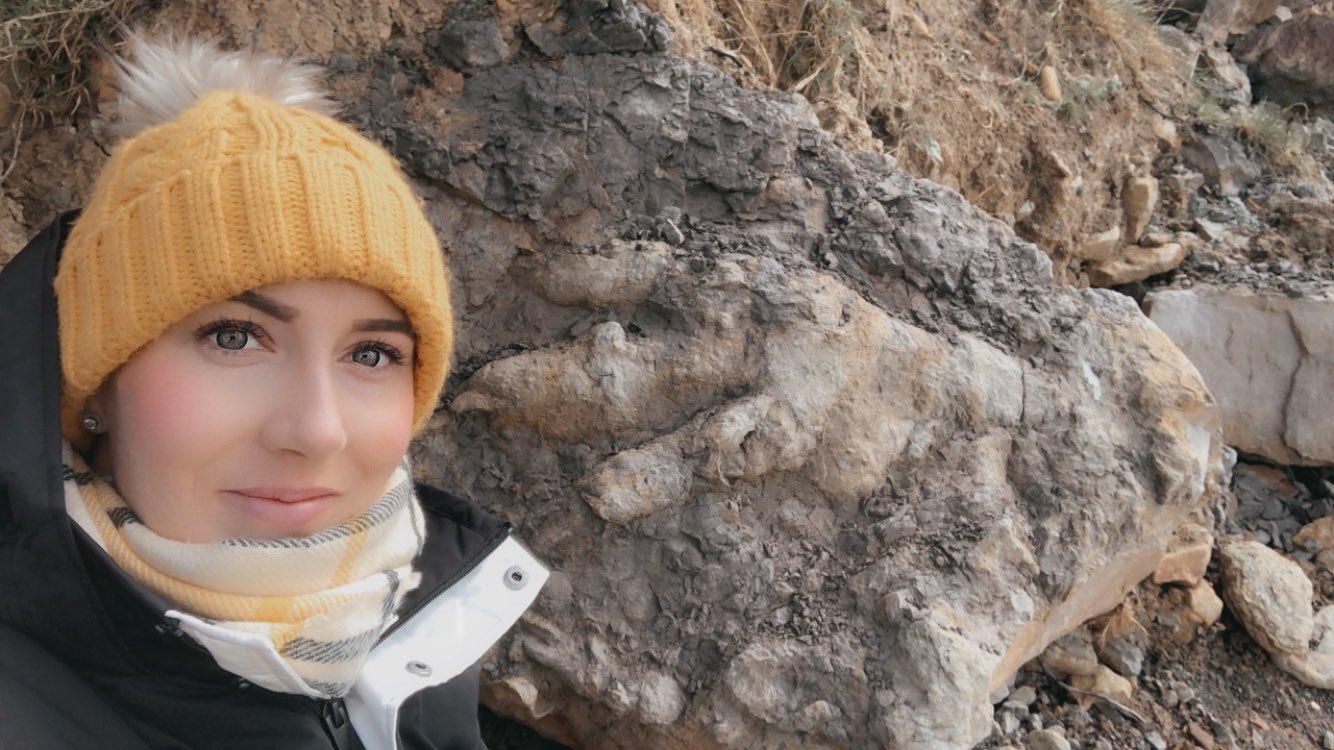 Woman standing beside a rock that has a three-toed footprint from a dinosaur on it