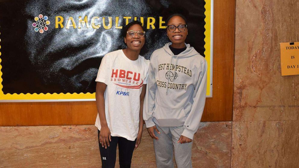Gloria and Victoria Guerrier, twin sisters from New York, stand in front of a poster in their school hallway.