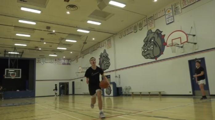 Kieran, wearing a black t-shirt, holds a basketball in his left hand as he runs up to the net.