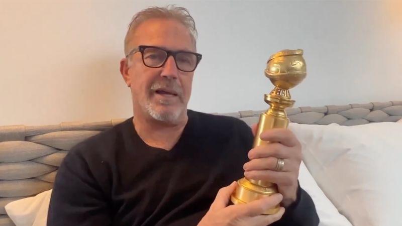 actor Kevin Costner sitting on couch holding a Golden Globe award