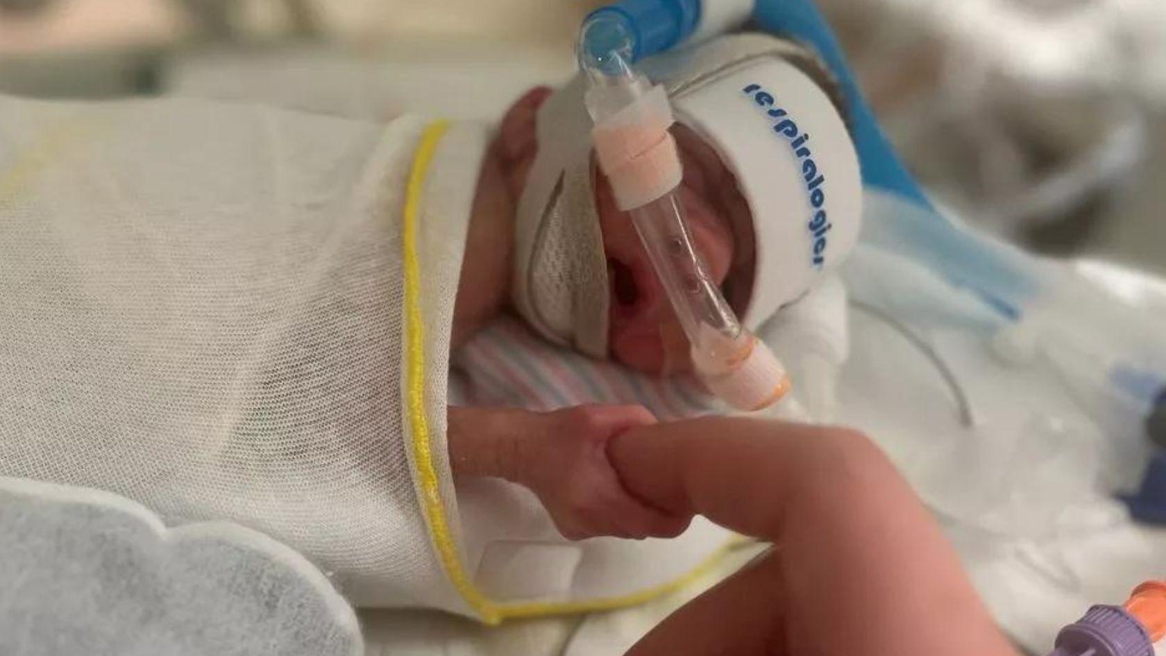 A newborn baby clutches a woman's finger