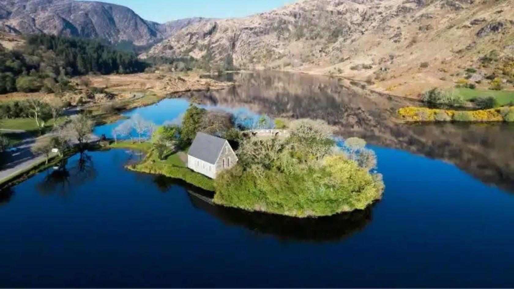 a house sits on a small island surrounded by water and mountains