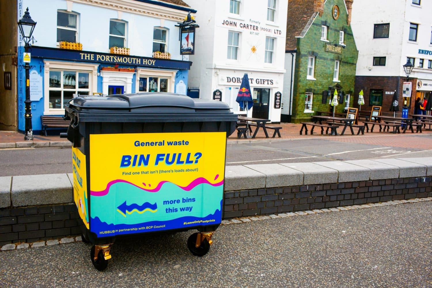 Yellow and turquoise garbage bin on wheels on UK street in front of a pub
