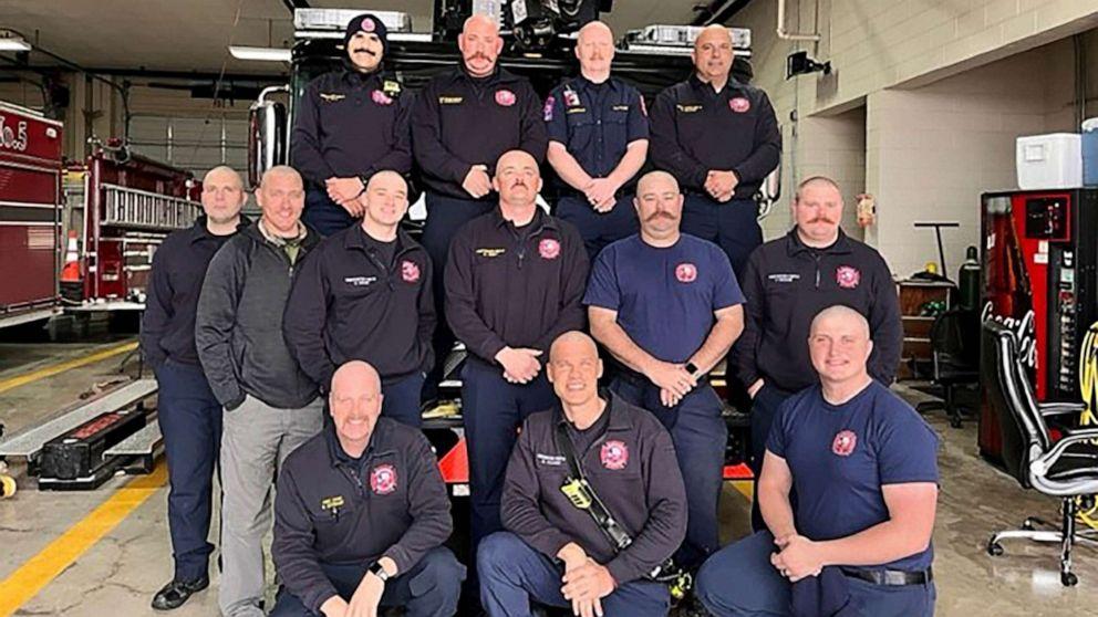 13 bald firefighters posing for a picture in front of a fire truck