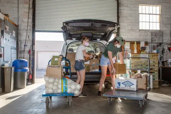 two people in a warehouse packing a van with boxes of leftover food