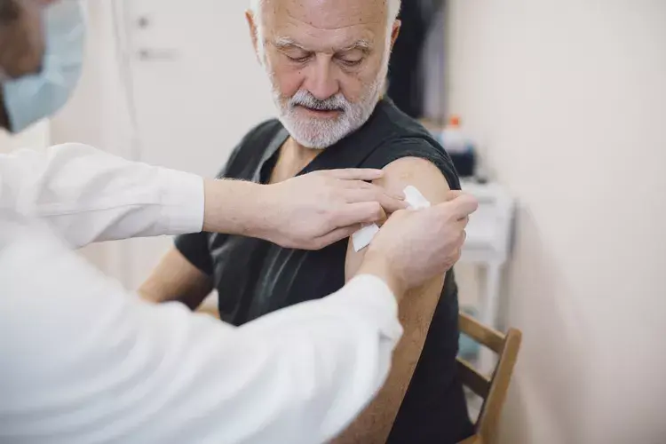 An elderly man receiving a bandaid on his shoulder form a nurse