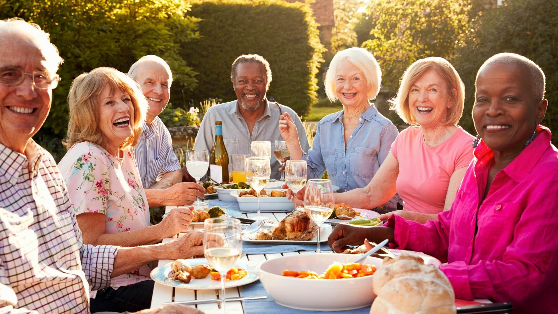 seniors sitting around a table, laughing and smiling in the sunshine while they are eating